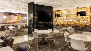 A modern hotel lobby with a bar area, seating arrangements, and a large mural on the wall.