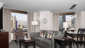 A modern hotel room with a grey sofa, a dining table, and a city view.