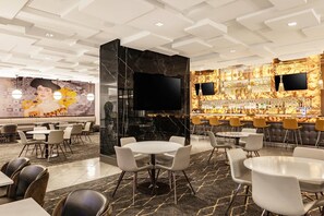 A modern hotel lobby with a bar area, seating arrangements, and a large mural.