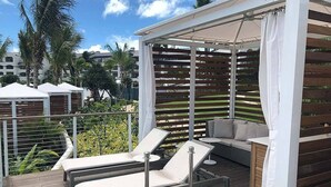 Un espacio de estar techado al aire libre con sillones y un sofá, rodeado por una terraza de madera y una barandilla metálica.