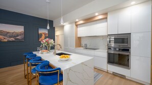 A modern kitchen with a marble island, stainless steel appliances, and blue bar stools. - Your luxury vacation begins here! (Drumheller)