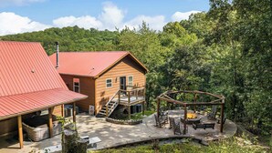 A cabin with a red roof, a wooden deck, and a fire pit area.