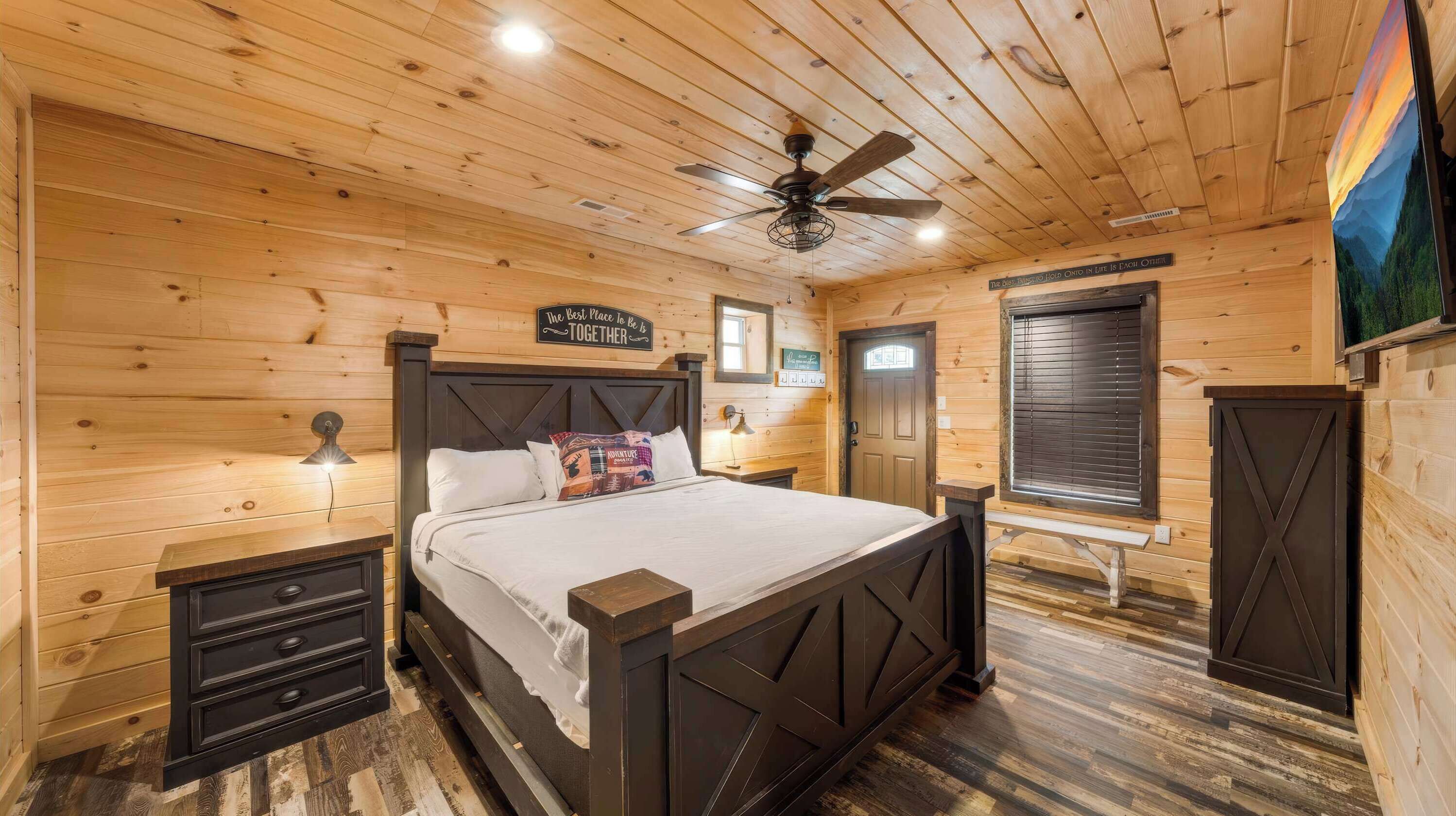 A wooden cabin bedroom with a bed, nightstands, a ceiling fan, and a window with blinds.