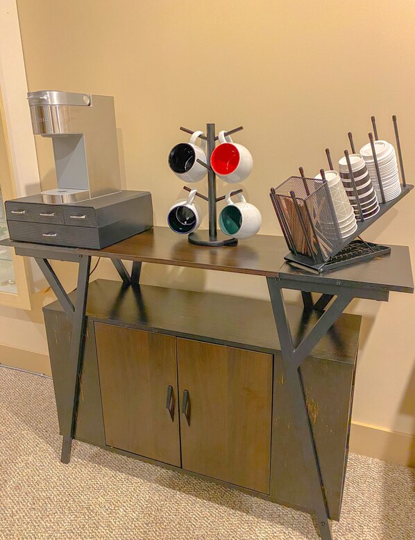 A kitchenette with a coffee machine, a mug rack, and a stack of plates.
