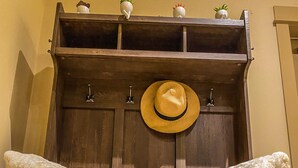 Un mueble de madera con dos almohadones blancos suaves, un sombrero de paja y tres macetas pequeñas con plantas.