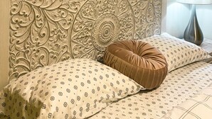 Un dormitorio con una cama que incluye un cabecero decorativo, un cuadro de paisaje enmarco y una lámpara de noche.