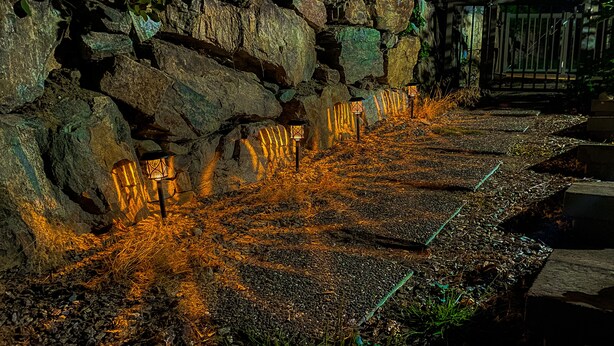 Un sendero con escalones de piedra y faroles, rodeado de rocas y vegetación.
