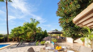 Une terrasse extérieure avec une piscine, des meubles en osier et une table dressée pour les repas.