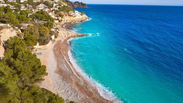 Une ville côtière avec des maisons construites sur une colline, d’où l’on a une vue imprenable sur une plage aux eaux turquoise.
