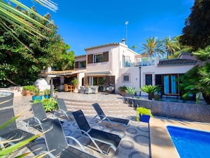 Una villa moderna con piscina, mobiliario de exterior y exuberante vegetación.