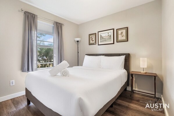 A neatly made bed with white linens, a bedside table with a lamp, and two framed pictures on the wall.