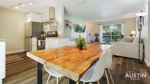 A modern kitchen with white cabinets, a stainless steel range hood, and a dining area with a wooden table and white chairs. - 5412 Pine xxxxxxxxxx (Austin)