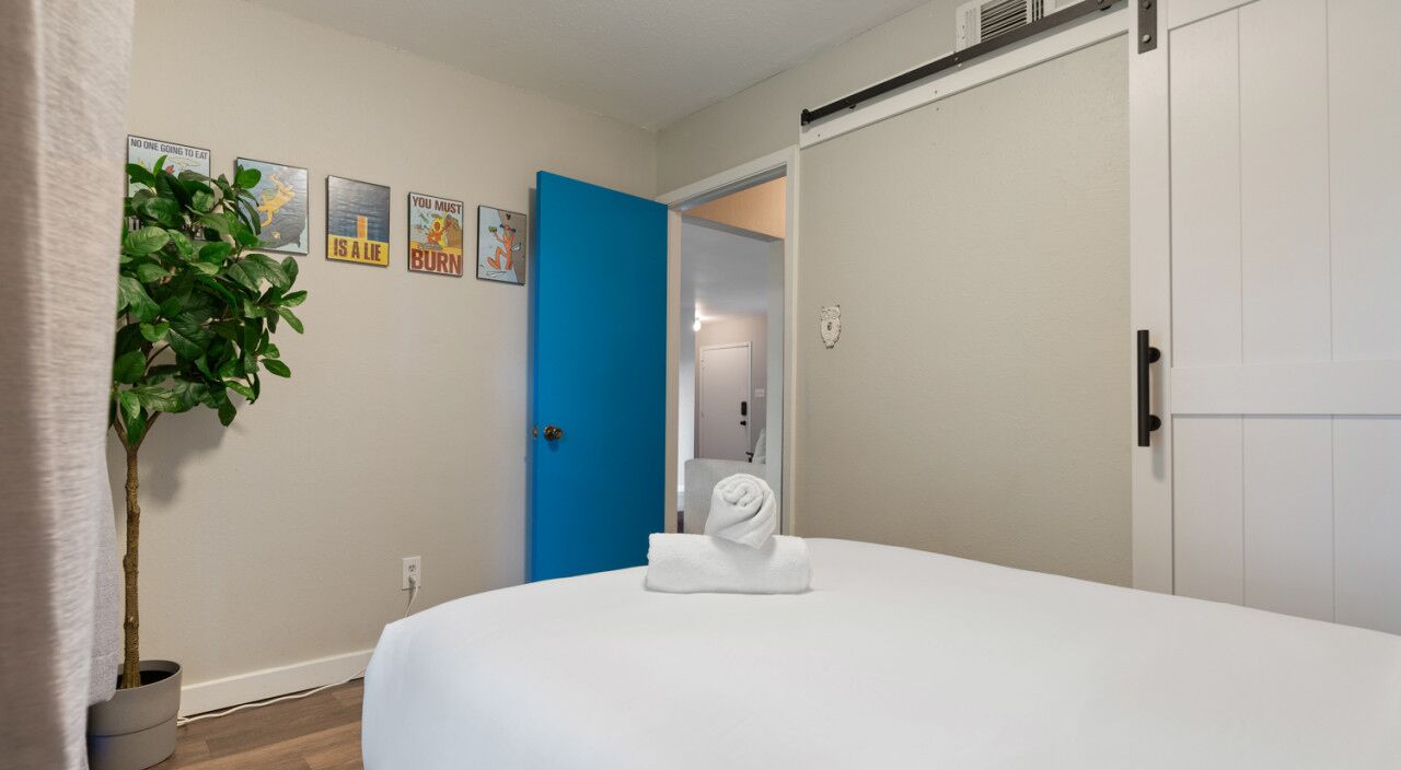 A bedroom with a bed, a blue door, a plant, and a towel on the bed.