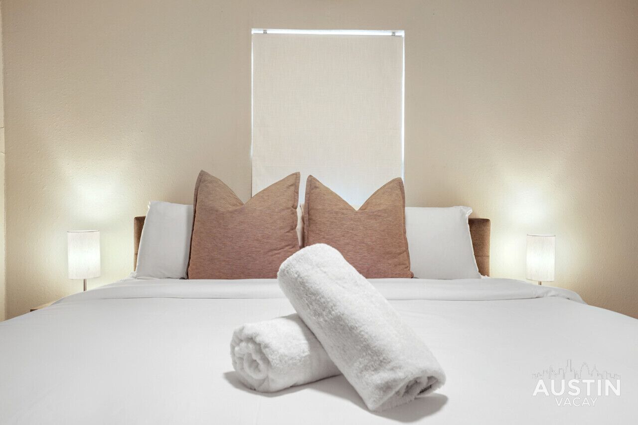 A hotel room with a neatly made bed, two bedside lamps, and a large window with a blind.