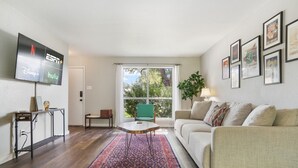 A living room with a flat-screen TV displaying streaming services, a green chair, a white sofa, a patterned rug, and framed pictures on the wall. - 5412 Pine xxxxxxxxxx (Austin)