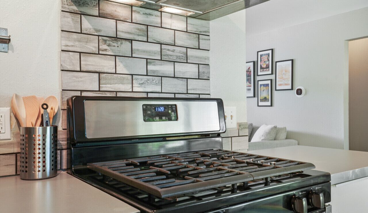 Een moderne keuken met een roestvrijstalen fornuis, een tegelwand van baksteen en een wit aanrecht.