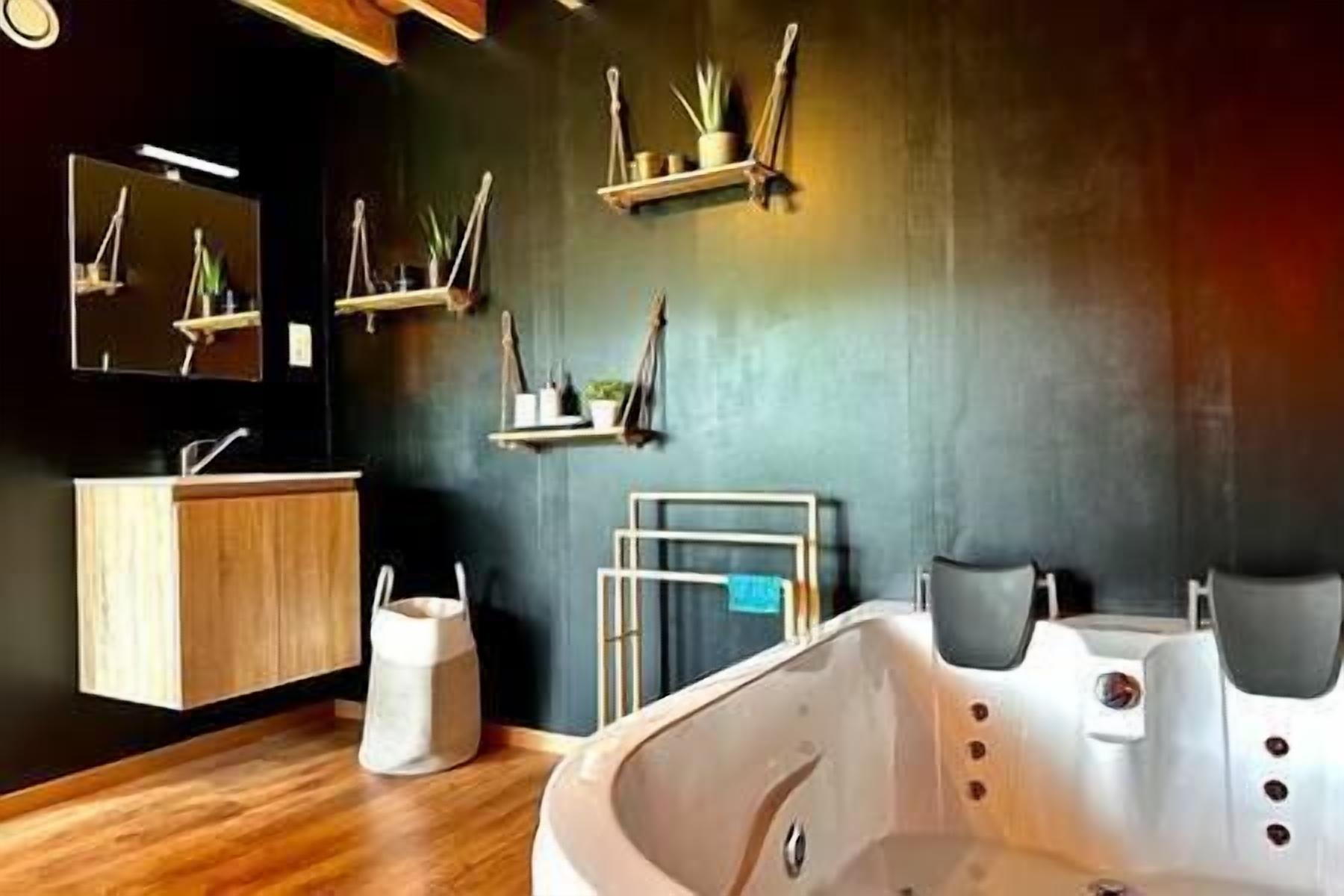 Une salle de bain moderne avec un meuble-lavabo en bois, une grande baignoire et des étagères remplies de produits de toilette.