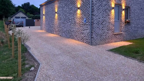 A brick building with a gravel driveway and a parking sign. - Hour House 2 - Honeymoon (Houyet)