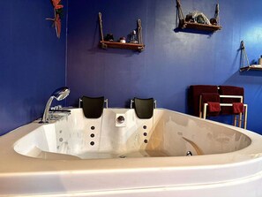 A large bathtub with two black chairs, a white sink, and a blue wall with shelves holding various items. - Hour House 2 - Honeymoon (Houyet)