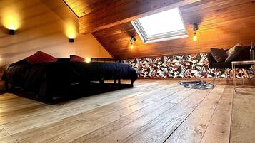 A high-ceilinged room with a sloped wooden ceiling, a skylight, a bed with a red pillow, a patterned wall, and a small round rug.