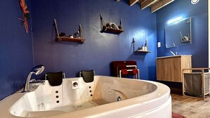 A modern bathroom with a large bathtub, wooden shelves, a red chair, and a wooden vanity. - Hour House 2 - Honeymoon (Houyet)