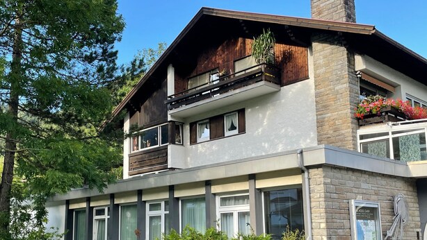 A modern two-story house with a balcony, large windows, and a stone facade.