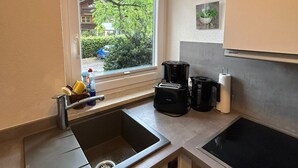 A compact kitchen with a sink, a coffee maker, and a toaster. There is a window with a view of greenery outside.