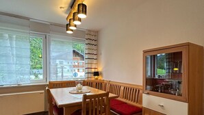 A dining area with a wooden table and benches, a cabinet with glass doors, and a window with blinds.