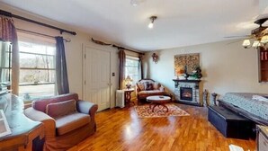 Ein gemütliches Wohnzimmer mit Holzboden, einer Couch, einem Sessel, einem Kamin und einem Bett.
