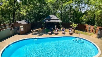 A swimming pool with lounge chairs and a gazebo in a shaded area surrounded by trees.