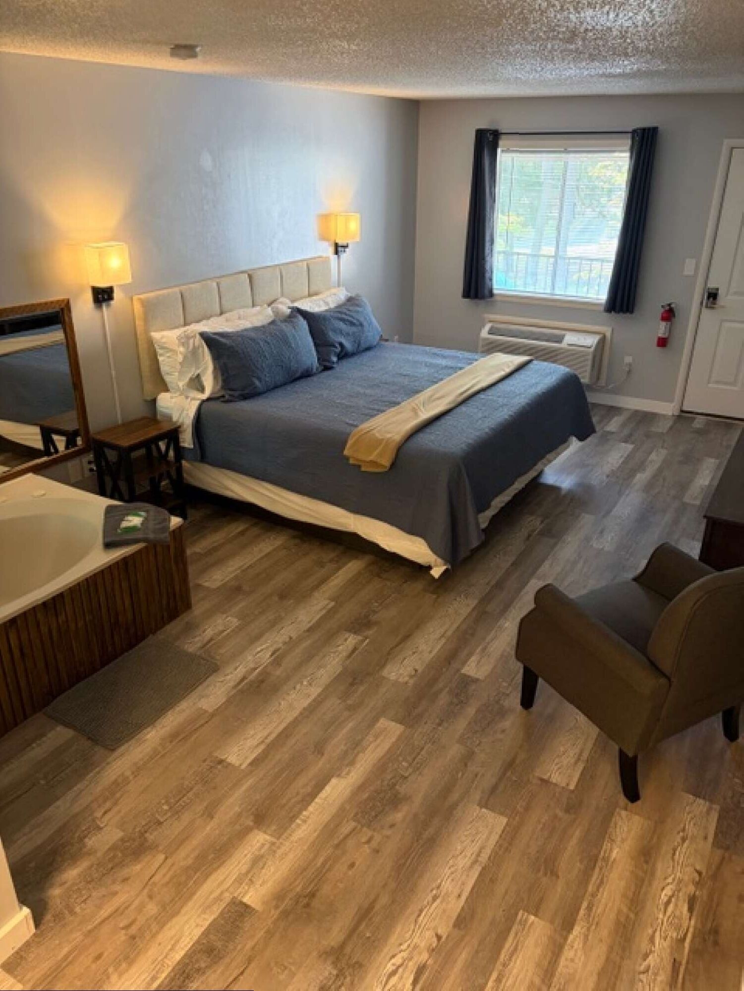 A bedroom with a bed, bedside lamps, a chair, a small table, and a window.