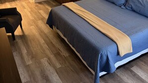 Een slaapkamer met een groot bed, een houten vloer, een badkamer met een bad en een spiegel.