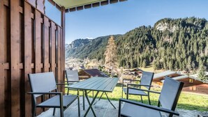 Eine Holzterrasse mit Tisch und Stühlen, mit Blick auf eine gebirgige Landschaft mit Häusern.