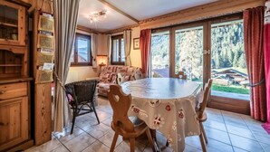 Ein Essbereich mit einem runden Tisch, Stühlen und Blick auf einen Wald durch große Fenster.