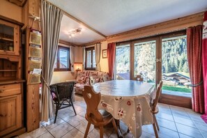 Un coin repas avec une table ronde, des chaises et une vue sur une forêt, visible à travers de grandes fenêtres.