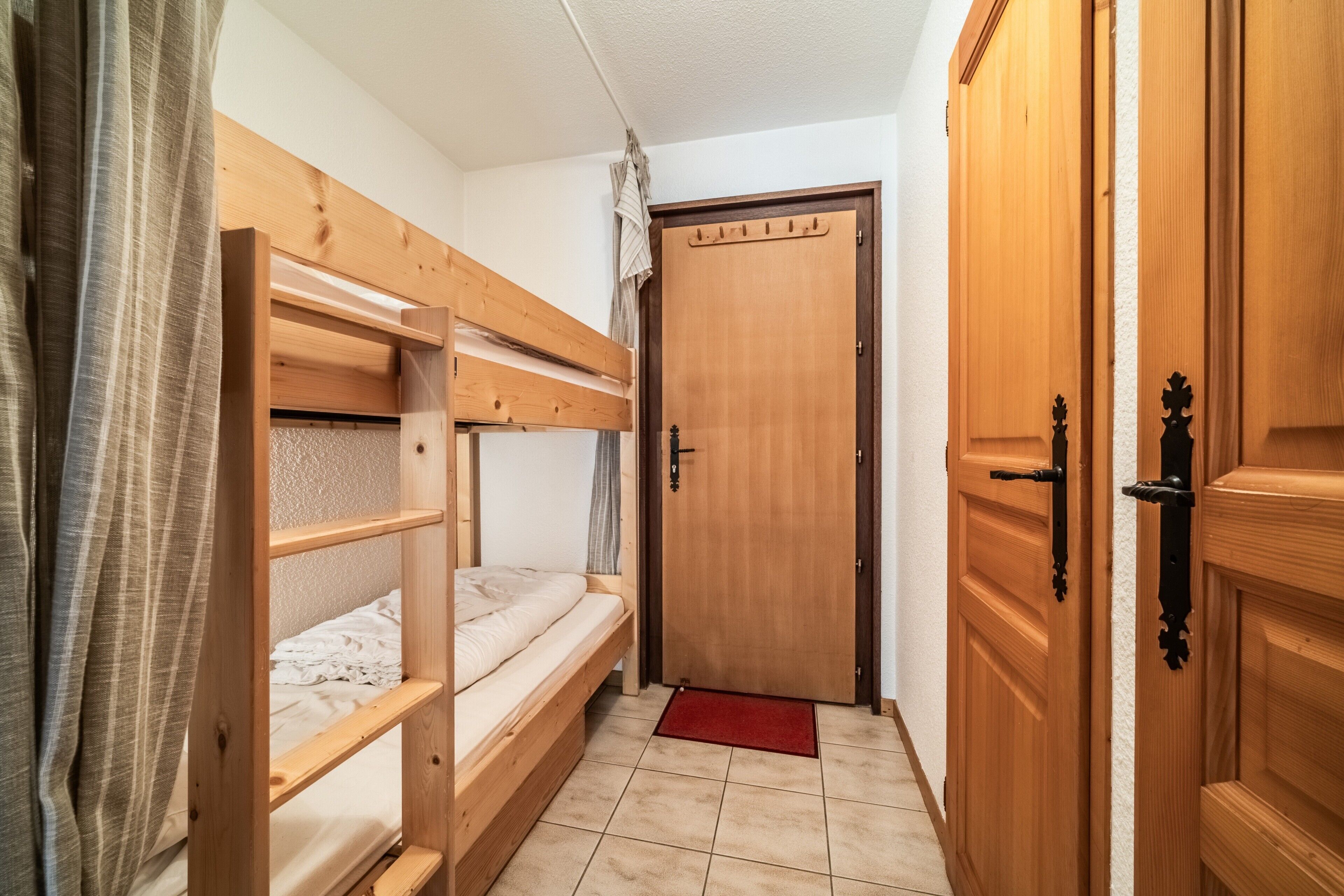 Een kamer met stapelbedden, een houten deur en een betegelde vloer.