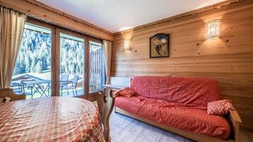 L’intérieur d’un chalet en bois, avec un canapé rouge, une table à manger et une vue sur une forêt, visible à travers de grandes fenêtres.