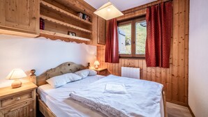 A wooden room with a bed, two bedside tables with lamps, a window with red curtains, and a shelf with books. - T3 Chatel Apartment with Mountain View, Private Terrace and Balcony (chatel)