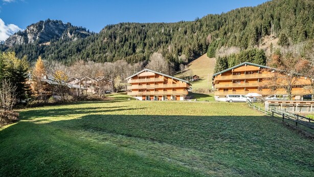 A mountain lodge with two wooden buildings, a grassy field, and a forested mountain backdrop. - Studio 'Châtel - At the Foot of Linga' with Mountain View and Balcony (Châtel)