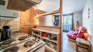 A compact kitchen with a stove, shelves, and a dining area with a bench. - Studio 'Châtel - At the Foot of Linga' with Mountain View and Balcony (Châtel)