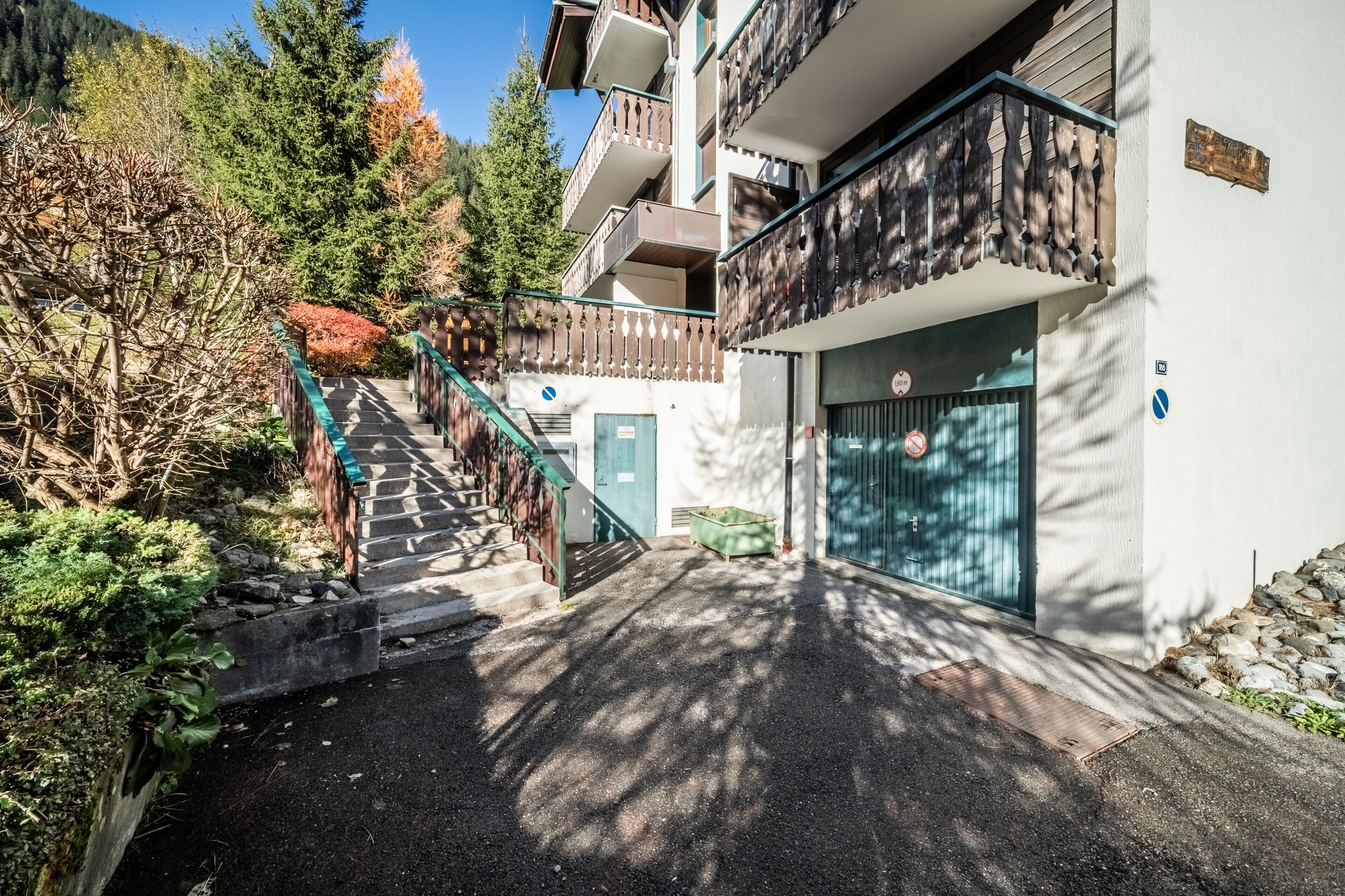 A building with a staircase leading to a balcony, a door with a sign, and a stone wall.
