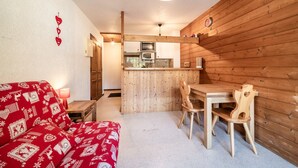 A compact kitchen with wooden walls, a dining area with a table and chairs, and a red patterned sofa. - Studio 'Châtel - At the Foot of Linga' with Mountain View and Balcony (Châtel)