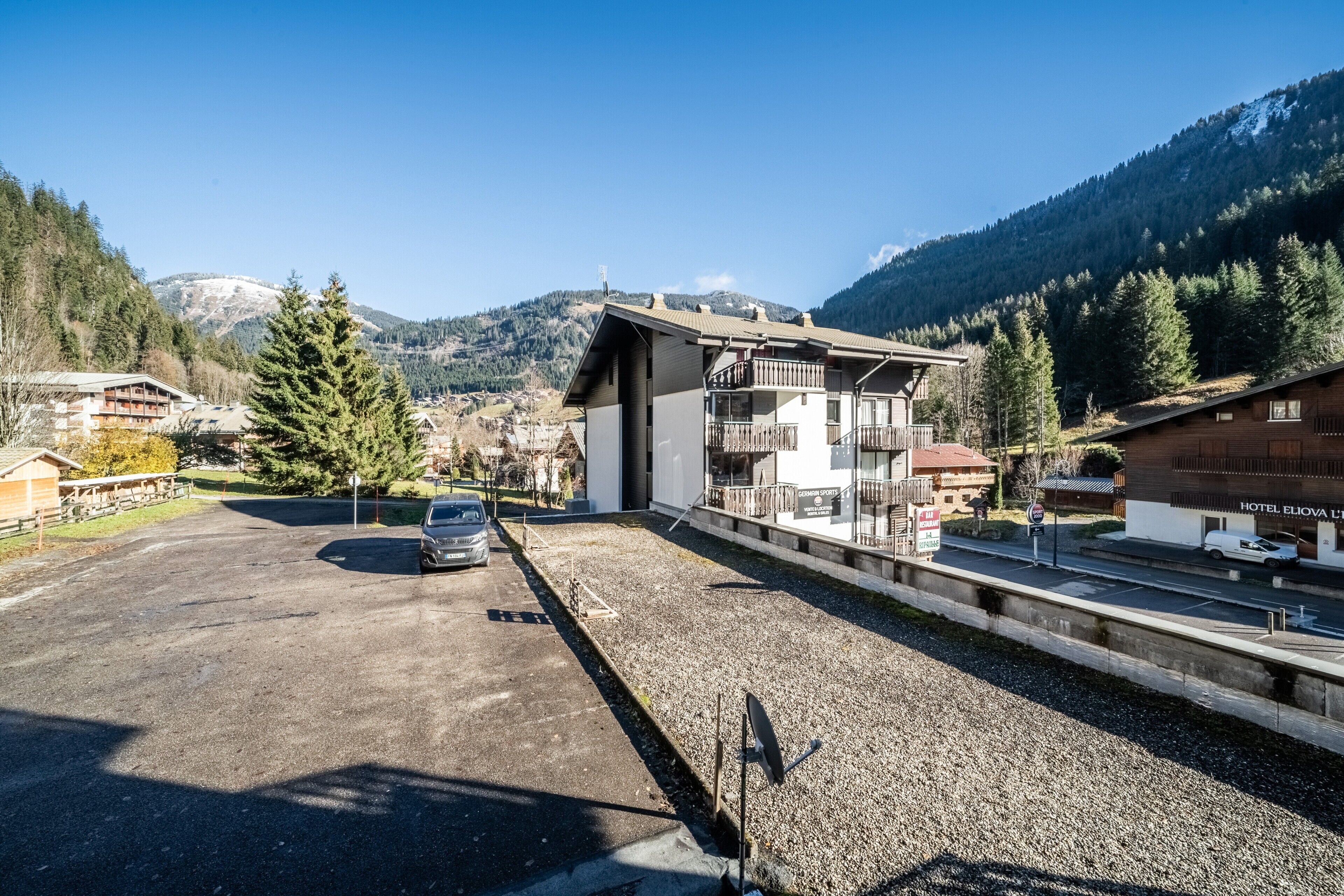 A hotel with a modern design, a parking area, and a view of mountains.