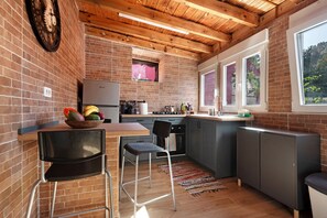 A kitchen with a brick wall, wooden ceiling beams, a window, and a bowl of fruit on the counter.