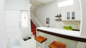 A compact kitchen with a white countertop, wooden stools, a sink, and cabinets. - Omah Bondi Family Homestay by FH Stay (Yogyakarta)