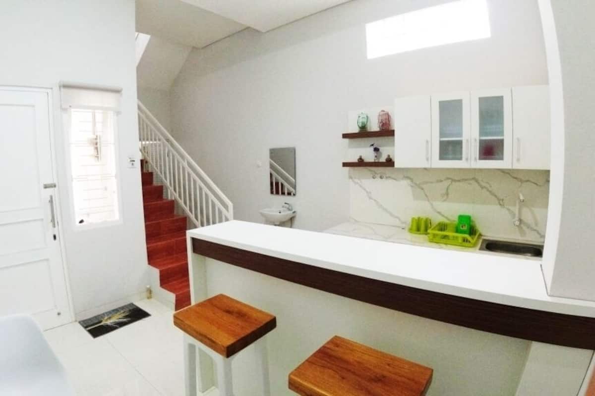 A compact kitchen with a white countertop, wooden stools, a sink, and cabinets.