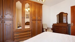 Een slaapkamer met een grote houten garderobe, een bed met een gewatteerde spreideken en een stoel.