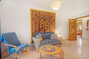 A living room with a sofa, a blue armchair, a small table, and a tapestry.