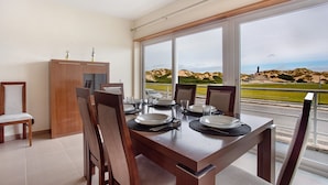 Een eetruimte met een tafel voor vier personen, grote ramen met uitzicht op een golfbaan en een houten kast.