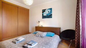 Une chambre à coucher comprenant un lit, une tête de lit, une œuvre d’art accrochée au mur, une chaise et une armoire.